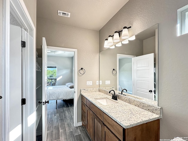 ensuite bathroom with visible vents, a textured wall, ensuite bath, wood tiled floor, and vanity