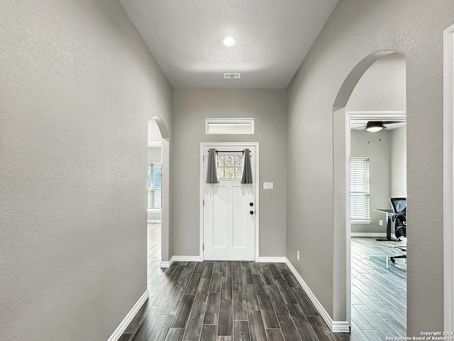 entrance foyer with arched walkways, a textured wall, dark wood-style floors, and visible vents