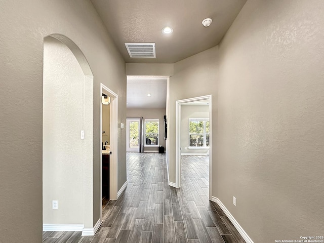 hall with baseboards, visible vents, arched walkways, a textured wall, and dark wood-type flooring