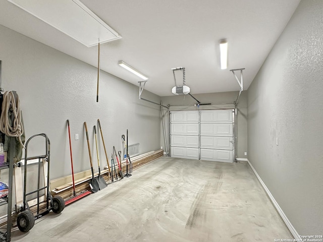 garage with a garage door opener, a textured wall, and baseboards