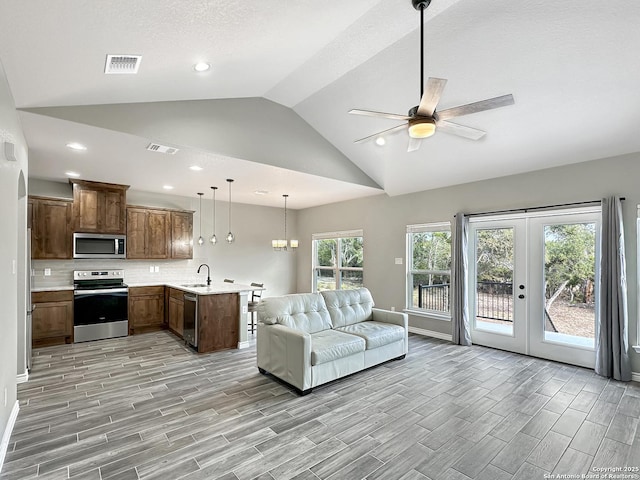 living area featuring wood finish floors, french doors, lofted ceiling, visible vents, and ceiling fan with notable chandelier