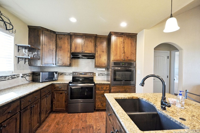 kitchen featuring tasteful backsplash, dark wood-style floors, appliances with stainless steel finishes, under cabinet range hood, and a sink