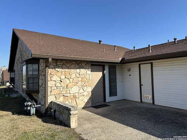 property entrance with stone siding, roof with shingles, and a patio area