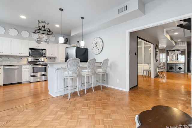 kitchen featuring stainless steel appliances, visible vents, white cabinetry, light countertops, and backsplash