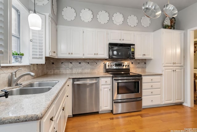 kitchen featuring light wood finished floors, decorative backsplash, stainless steel appliances, white cabinetry, and a sink