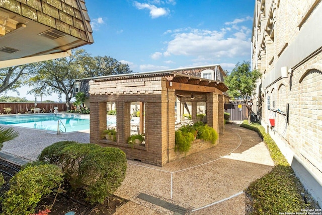 exterior space with brick siding, an outdoor structure, a fenced backyard, and a community pool