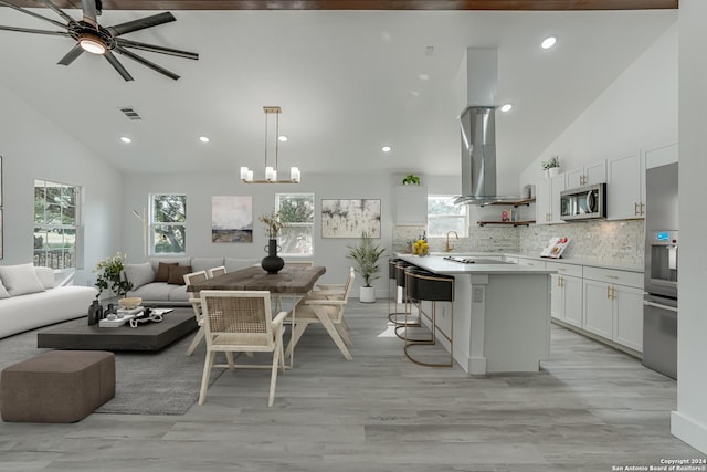 kitchen with a breakfast bar area, white cabinets, open floor plan, stainless steel microwave, and island exhaust hood