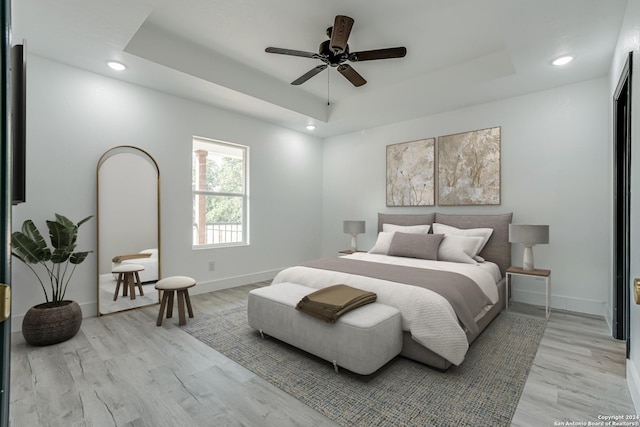 bedroom with light wood-style floors, a tray ceiling, and baseboards