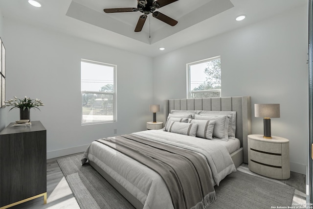 bedroom with baseboards, a ceiling fan, light wood-style flooring, a tray ceiling, and recessed lighting