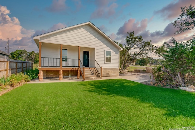 back of property featuring covered porch, a lawn, and fence