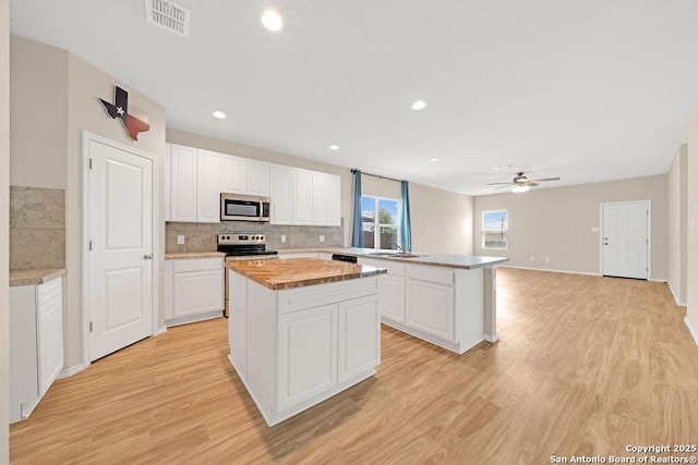 kitchen featuring light wood finished floors, visible vents, butcher block counters, appliances with stainless steel finishes, and a center island