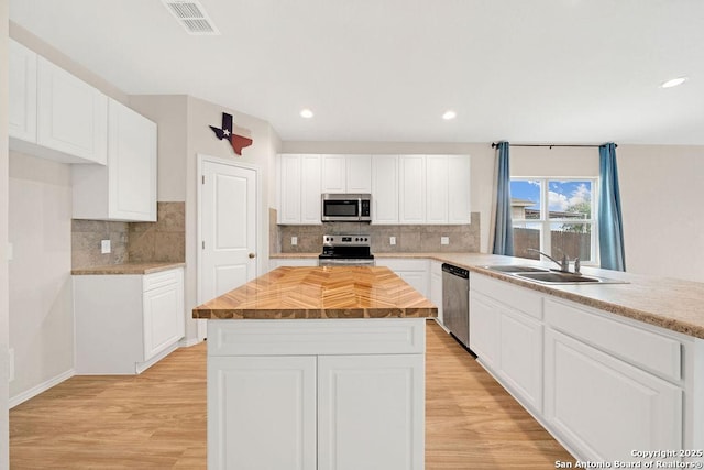 kitchen with light wood-style flooring, stainless steel appliances, a kitchen island, a sink, and visible vents