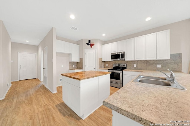 kitchen featuring light wood finished floors, visible vents, a kitchen island, appliances with stainless steel finishes, and a sink