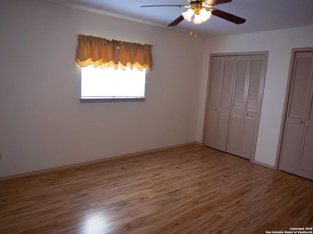 unfurnished bedroom with wood finished floors, a ceiling fan, and multiple closets