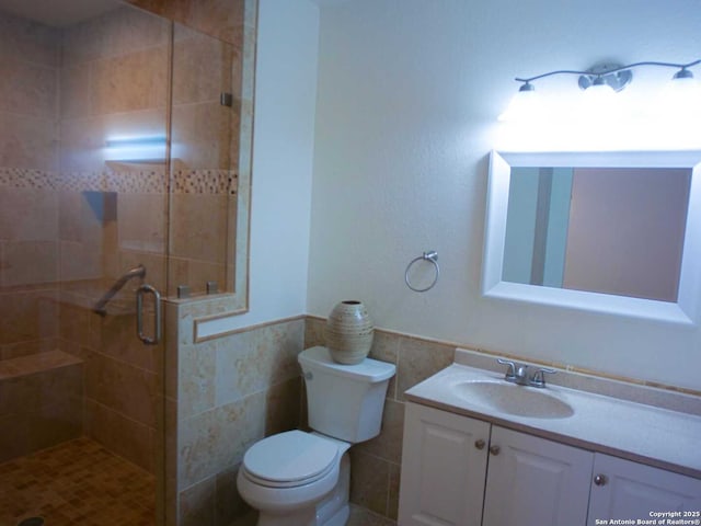 full bath featuring toilet, vanity, tile walls, wainscoting, and a stall shower