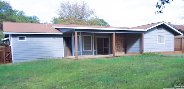 back of house featuring stone siding, a lawn, and fence