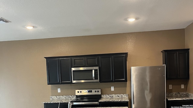 kitchen with stainless steel appliances, light stone countertops, visible vents, and dark cabinetry