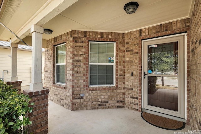 view of exterior entry featuring a porch and brick siding