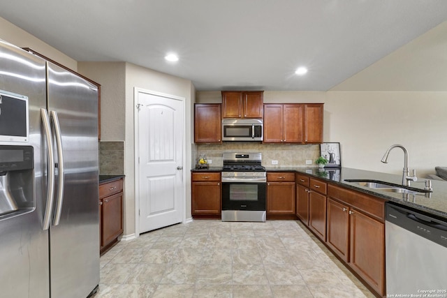 kitchen featuring tasteful backsplash, brown cabinetry, appliances with stainless steel finishes, dark stone countertops, and a sink