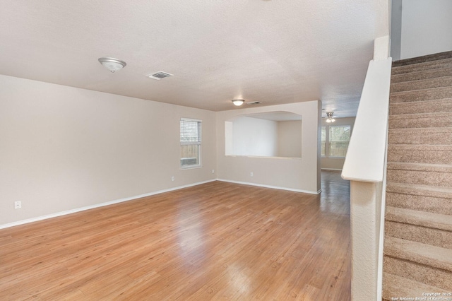 interior space featuring baseboards, visible vents, stairs, a textured ceiling, and light wood-type flooring