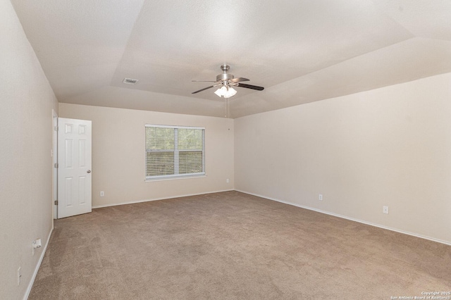 carpeted spare room featuring vaulted ceiling, a raised ceiling, a ceiling fan, and baseboards