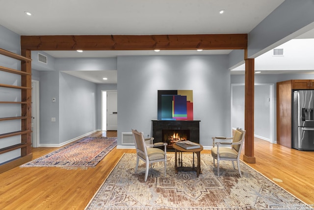 dining area featuring light wood-type flooring, visible vents, beamed ceiling, and a lit fireplace