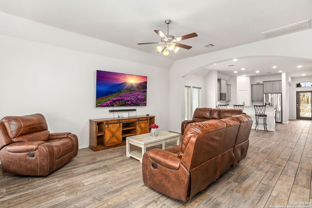 living area with arched walkways, a ceiling fan, visible vents, and light wood-style floors