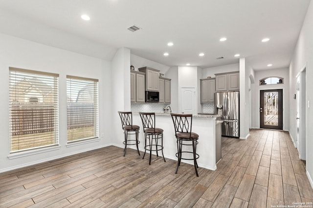 kitchen with gray cabinetry, a peninsula, visible vents, tasteful backsplash, and stainless steel fridge