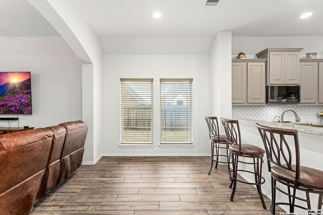 kitchen featuring wood finished floors, stainless steel microwave, decorative backsplash, and gray cabinetry