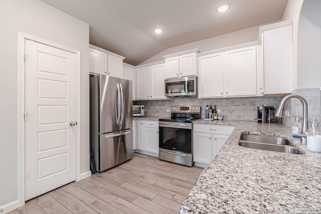 kitchen with lofted ceiling, stainless steel appliances, a sink, white cabinets, and backsplash