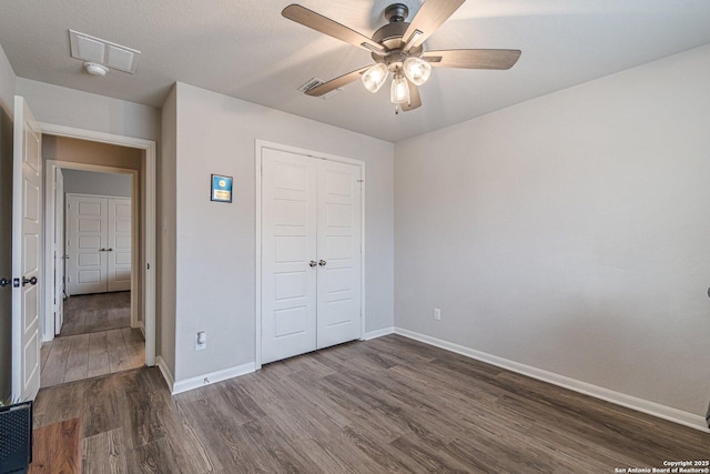 unfurnished bedroom featuring visible vents, baseboards, a ceiling fan, dark wood-style floors, and a closet