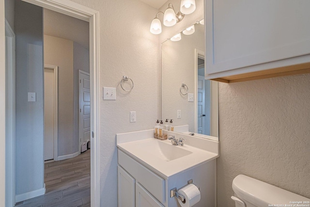 half bathroom featuring a textured wall, vanity, toilet, and wood finished floors