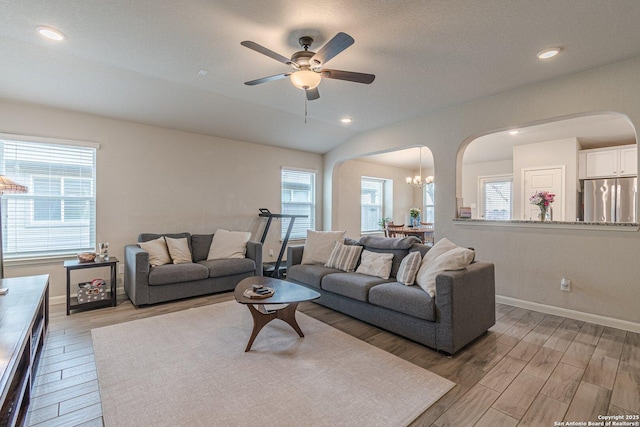 living area featuring light wood-type flooring, baseboards, arched walkways, and lofted ceiling