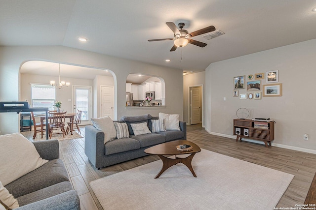 living room featuring arched walkways, light wood-style flooring, ceiling fan with notable chandelier, and visible vents