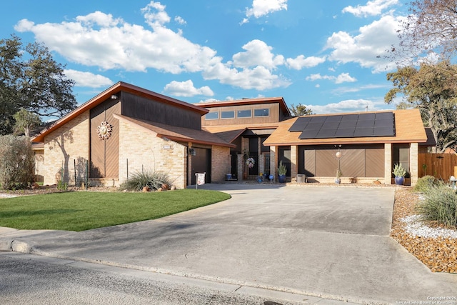 view of front of home featuring brick siding, concrete driveway, an attached garage, a front yard, and roof mounted solar panels