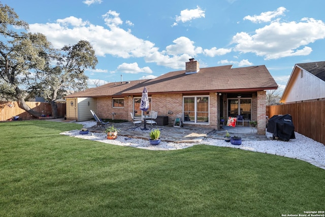 back of house with a yard, a patio, brick siding, and a fenced backyard