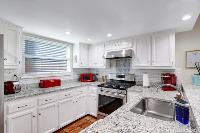 kitchen with decorative backsplash, under cabinet range hood, white cabinetry, a sink, and gas stove