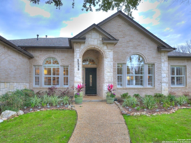 view of front of property featuring brick siding, roof with shingles, and a front lawn