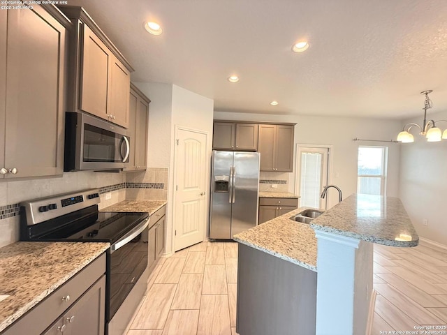 kitchen featuring stainless steel appliances, a sink, backsplash, light stone countertops, and an inviting chandelier