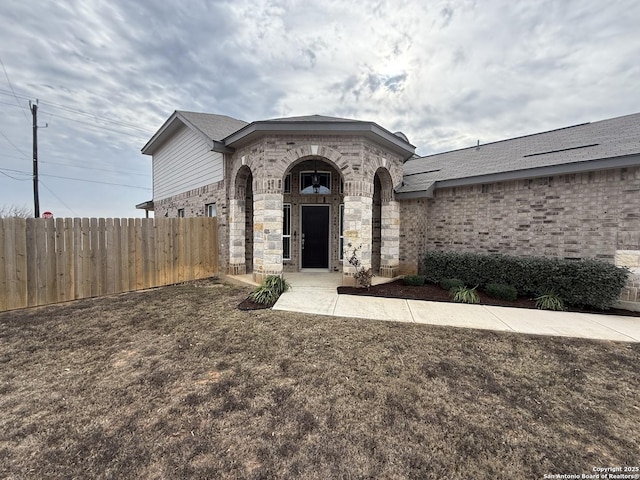 exterior space with brick siding, a shingled roof, and fence