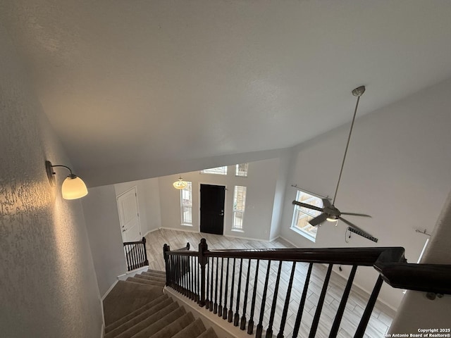 stairs with a ceiling fan, vaulted ceiling, baseboards, and wood finished floors