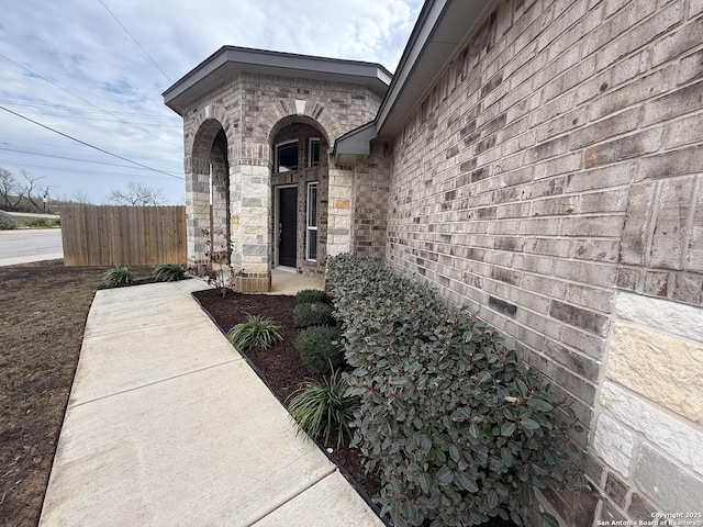 doorway to property featuring brick siding and fence