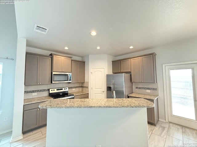 kitchen featuring a center island, visible vents, decorative backsplash, gray cabinetry, and appliances with stainless steel finishes