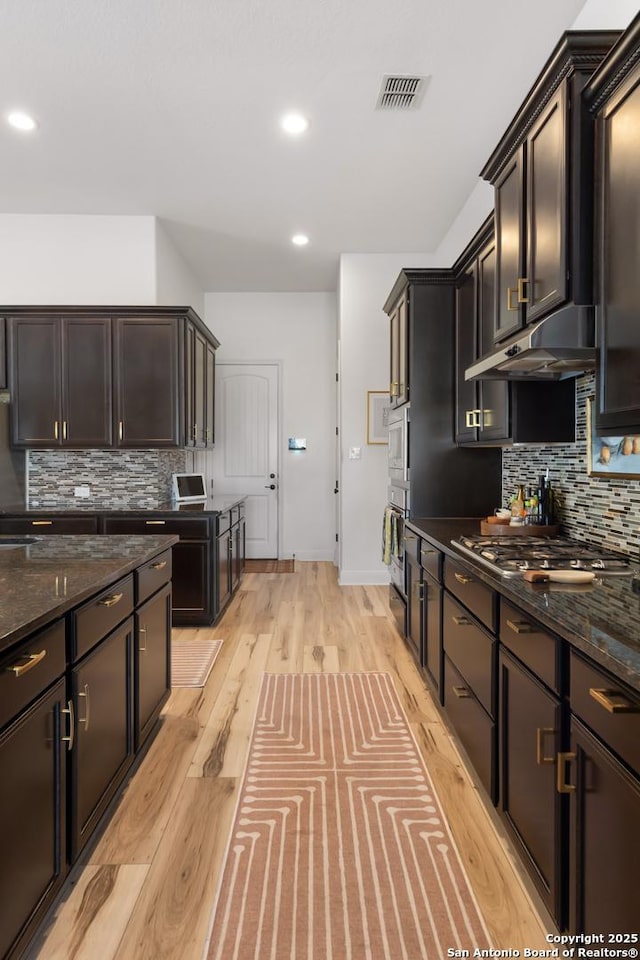 kitchen with under cabinet range hood, stainless steel appliances, visible vents, light wood-type flooring, and dark stone countertops