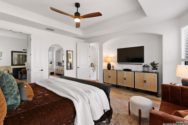 bedroom featuring visible vents, arched walkways, a raised ceiling, ceiling fan, and light wood-style floors