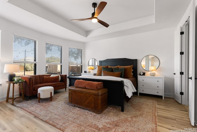 bedroom with baseboards, ceiling fan, a tray ceiling, and light wood-style floors