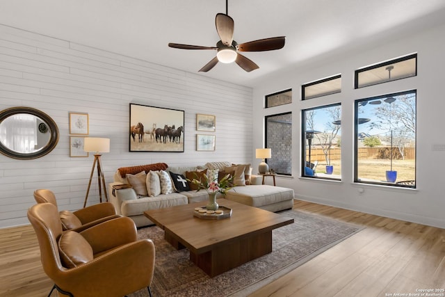 living area with light wood finished floors, a ceiling fan, and baseboards