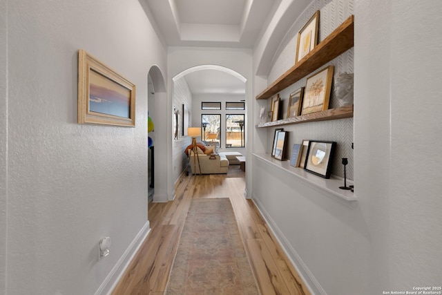 corridor with arched walkways, light wood-style flooring, and baseboards