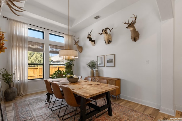 dining area featuring a tray ceiling, visible vents, baseboards, and wood finished floors