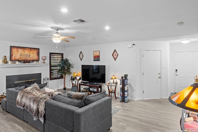 living room featuring light wood-type flooring, visible vents, a tiled fireplace, and recessed lighting